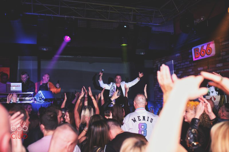 Zatłoczony parkiet z rękami w górze pod neonem B66